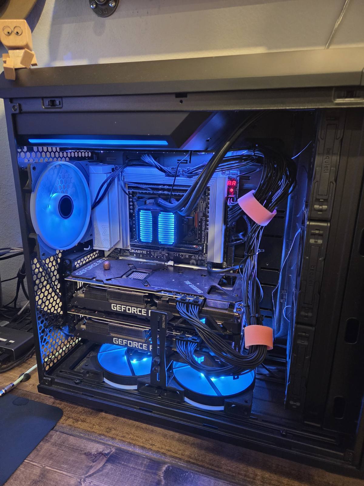 Inside the workstation: a TRX50 motherboard, dual GeForce RTX GPUs, and blue-lit memory behind a large air cooler.