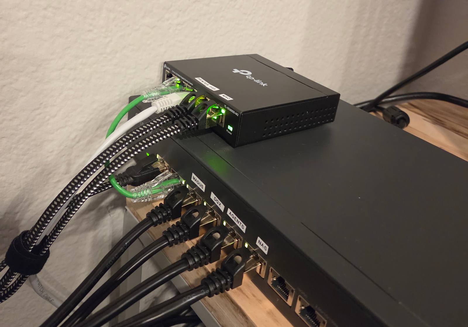 A 10-gigabit switch with ports hand-labeled MAGUS, DGX, AGENTS, and NAS, black and green cables plugged in.
