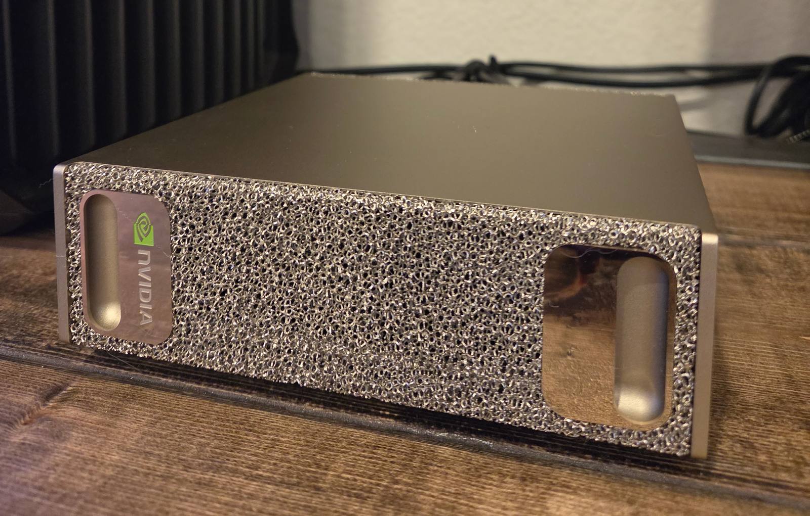 The NVIDIA DGX Spark: a compact gold chassis with a porous metallic-foam front panel and the NVIDIA logo, on a wooden desk.