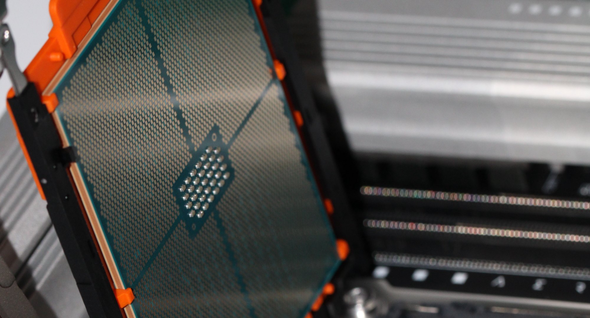 Macro photograph of the Threadripper processor die in its orange carrier, lifted above the open motherboard socket, the silicon catching the light.